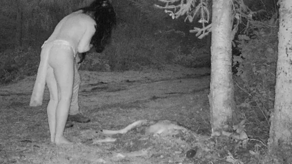 Las piernas de un hombre aparecen detrás de una figura capturada por Stanhope en su cámara de rastreo comiendo un ciervo muerto.